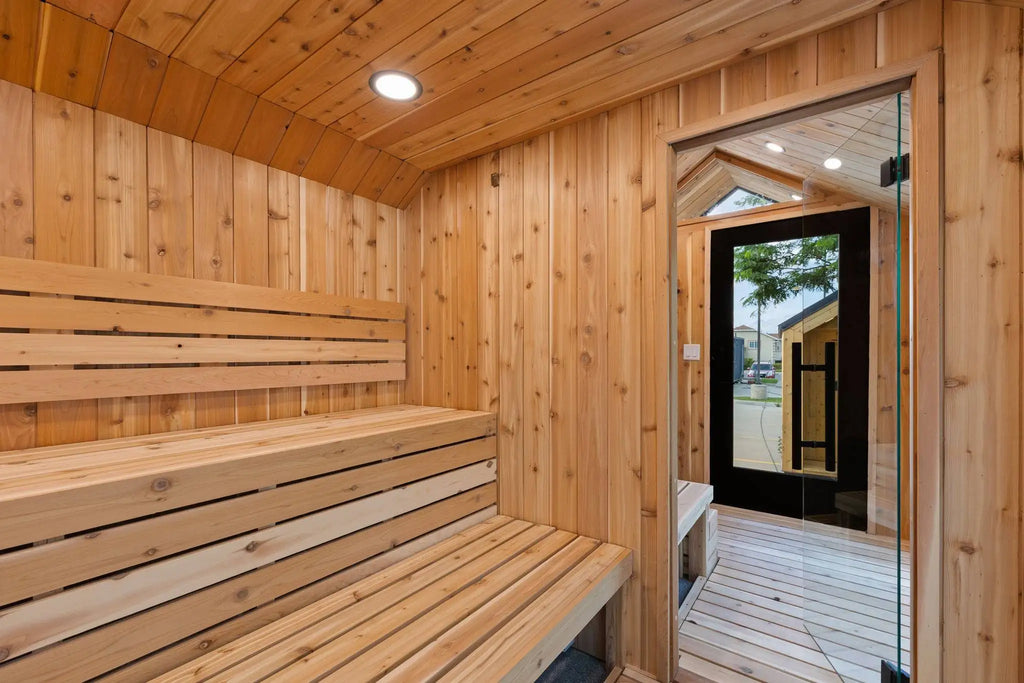 A wooden sauna interior with tiered wooden benches, wood-paneled walls and ceiling, recessed lighting, and a glass door opening to an outdoor deck.
