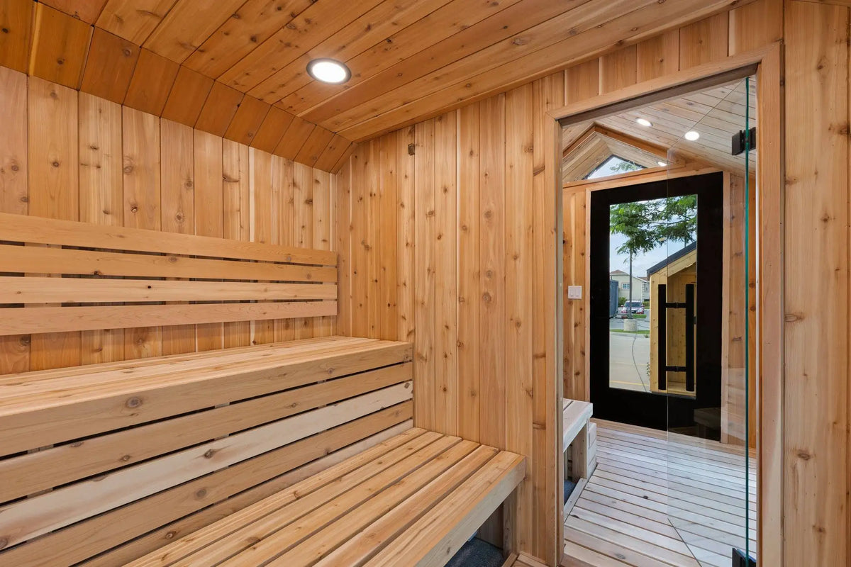 A wooden sauna interior with tiered wooden benches, wood-paneled walls and ceiling, recessed lighting, and a glass door opening to an outdoor deck.