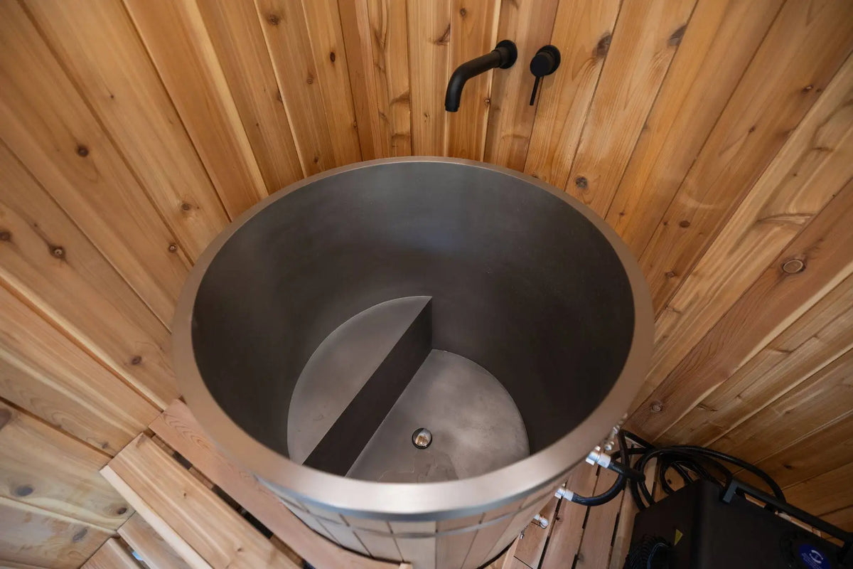 A large stainless steel sauna tub with a two-compartment divider, set inside a wooden sauna with wood-paneled walls and floor.
