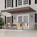 A brown retractable patio awning extends over a dining area on a house porch. The scene shows a gray brick home exterior with white-framed windows, black shutters, outdoor lanterns, a wooden dining table, and black mesh chairs.