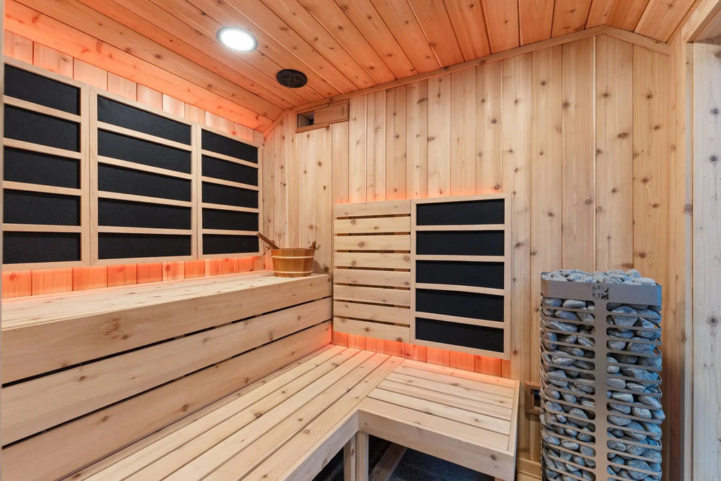 A wooden sauna interior with light natural wood walls and benches, black paneling, warm orange ambient lighting, a hanging stack of folded towels, and a visible wood-burning stove.