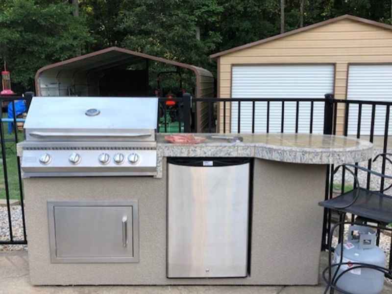 Outdoor kitchen setup with a grill and refrigerator on a patio