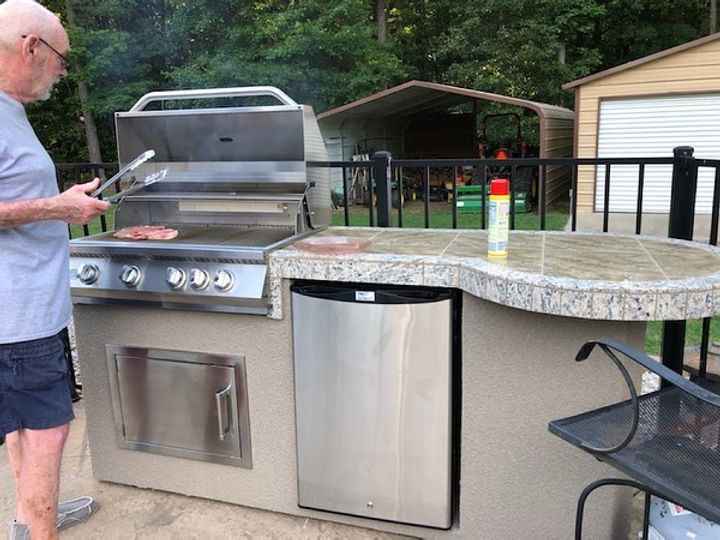 Man grilling outdoors on a patio with a barbecue and counter area.
