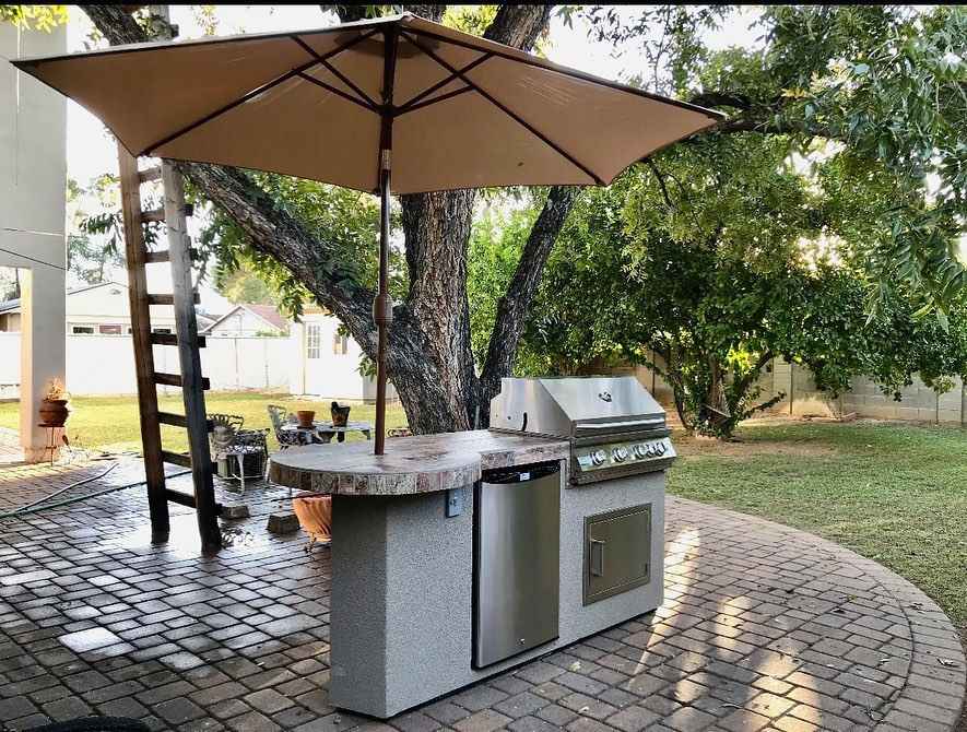 Outdoor kitchen setup with grill, table, and umbrella on a patio