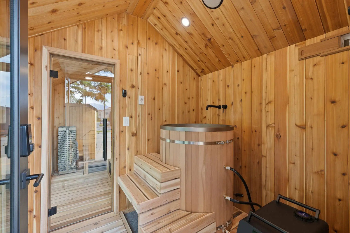 A rustic wooden sauna interior with a wooden hot tub, built-in wooden benches, wood-paneled walls and ceiling, and a glass door on the left.