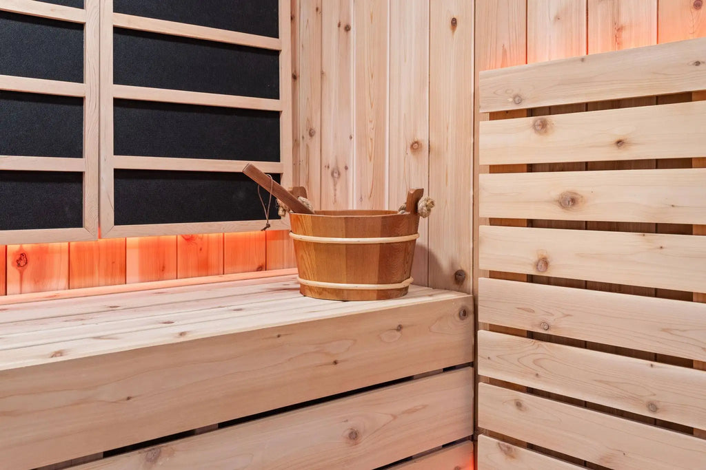 A traditional wooden sauna interior with light pine wood walls, a wooden bench, a wooden bucket, and a wooden ladle, illuminated by warm orange-red ambient lighting.