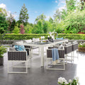 Outdoor patio set with table and chairs on a tiled patio area with greenery in the background.