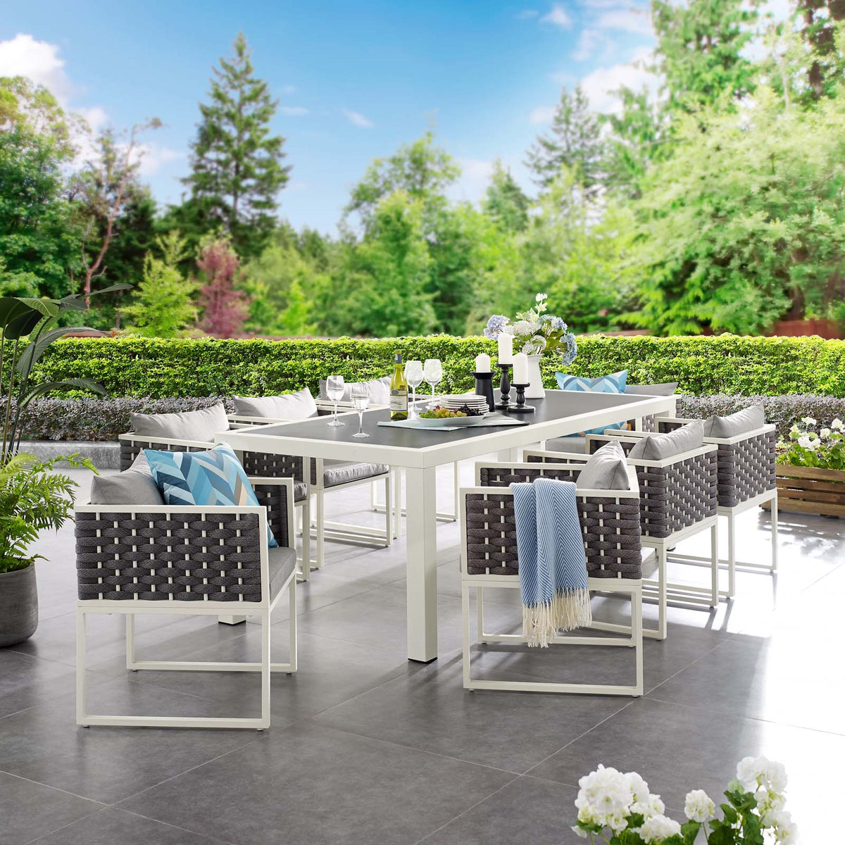 Outdoor patio set with table and chairs on a tiled patio area with greenery in the background.