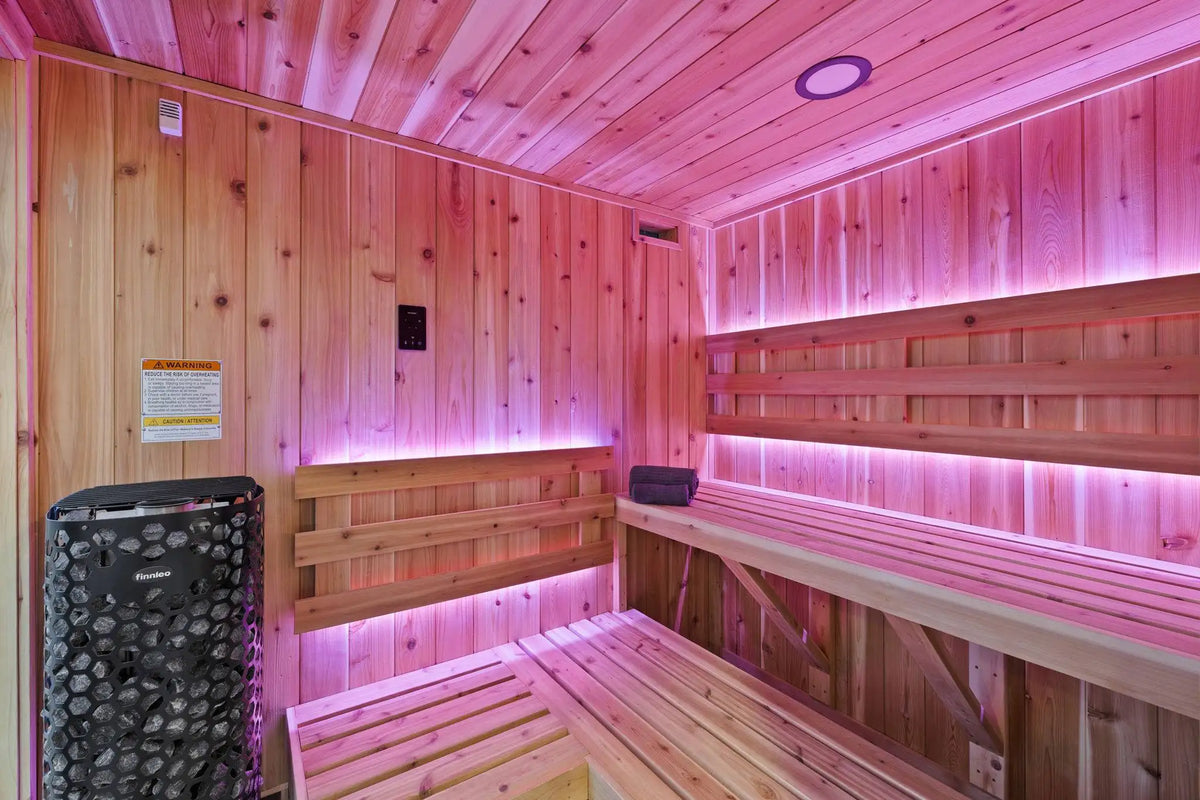 A wooden sauna interior with tiered wooden benches, wood-paneled walls and ceiling, pink ambient lighting, and a black sauna stove on the left side.