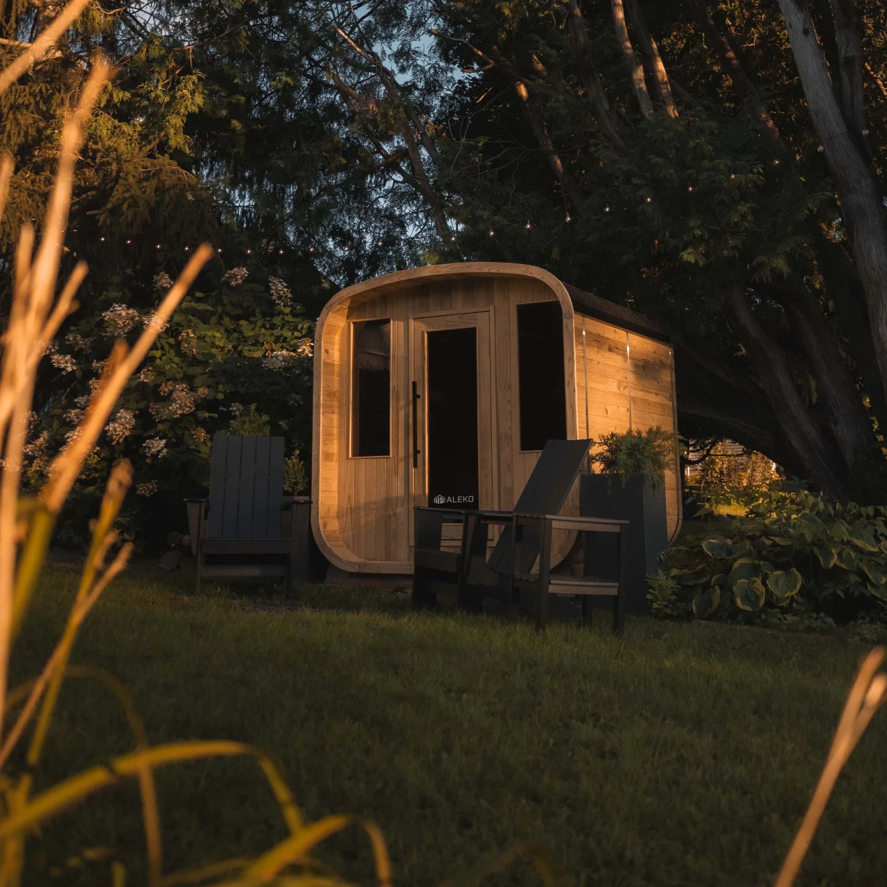 Wooden sauna in a garden setting with trees and grass.