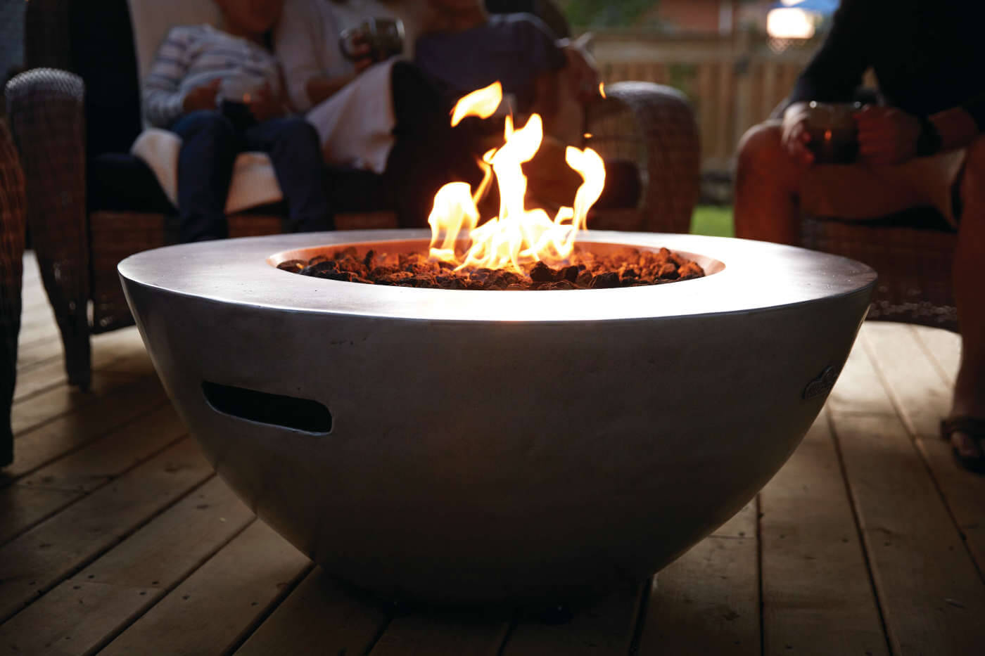 Fire pit with flames on a wooden deck, people sitting around
