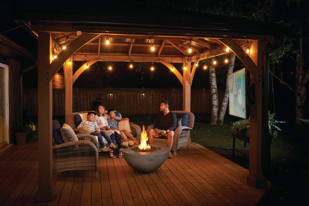 Family gathered around a fire pit under a wooden pergola at night.