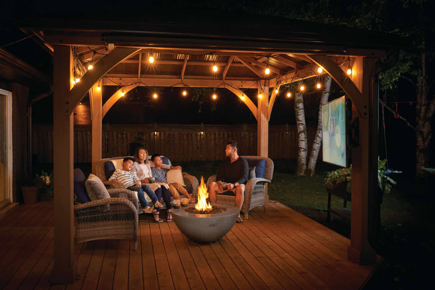 Family gathered around a fire pit under a wooden pergola at night.