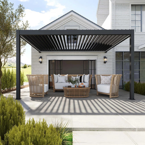 A modern outdoor pergola setup under a black pergola with wicker furniture, including a sofa, two armchairs, and a round coffee table, set against a white house background.
