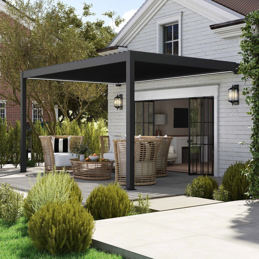 A modern black metal pergola with an attached outdoor dining area, set on a deck in front of a white brick house with sliding glass doors and landscaped greenery.