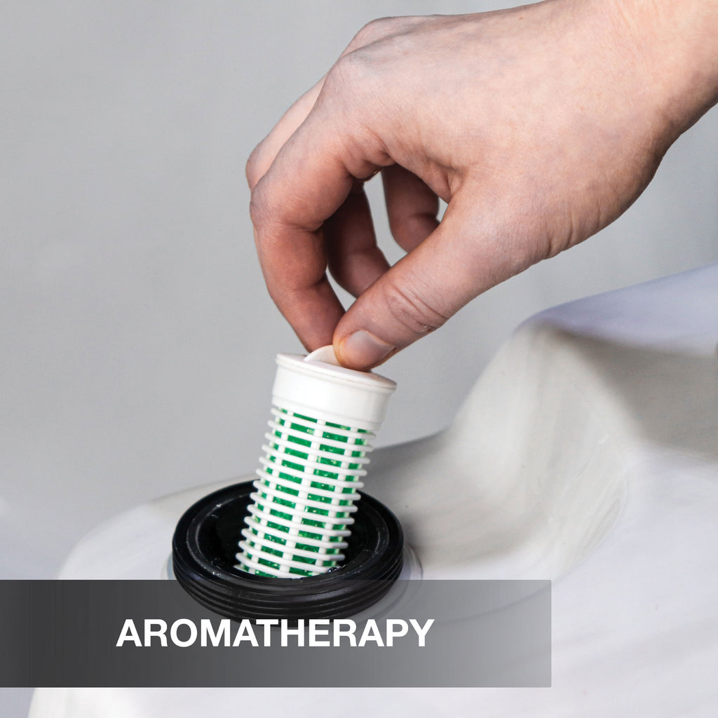 Hand placing a cylindrical green and white object into a white container with 'Aromatherapy' text.