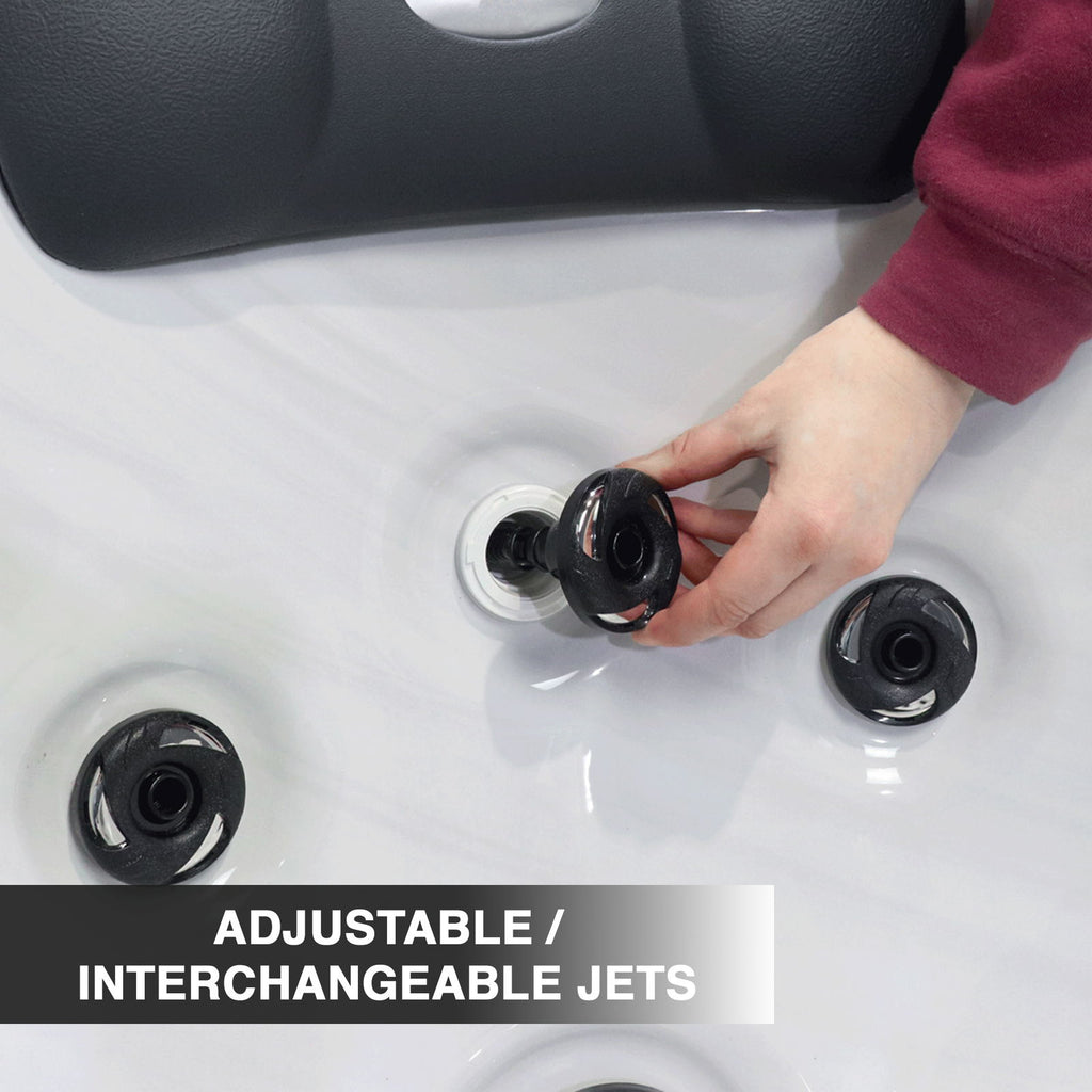 Hand adjusting an interchangeable jet on a hot tub with text 'Adjustable/Interchangeable Jets'.