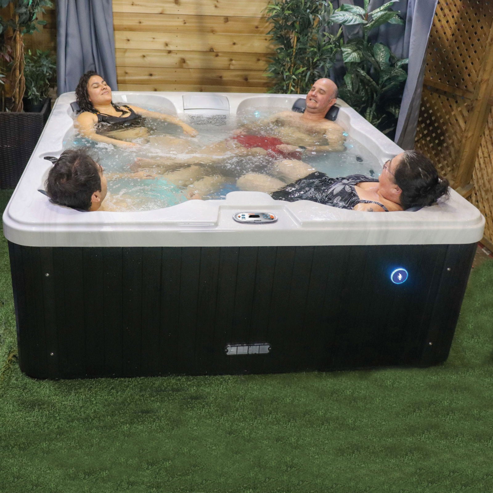 People relaxing in a hot tub outdoors with plants and wooden wall in the background