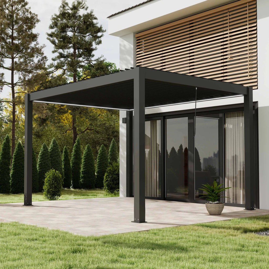 A modern black metal patio pergola with a slatted roof supported by four posts, extending over a paved patio area next to a house with glass doors, trees, and a lawn.