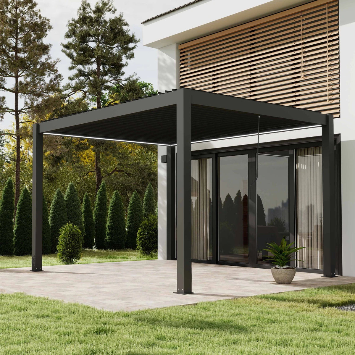 A modern black metal patio pergola with a slatted roof supported by four posts, extending over a paved patio area next to a house with glass doors, trees, and a lawn.