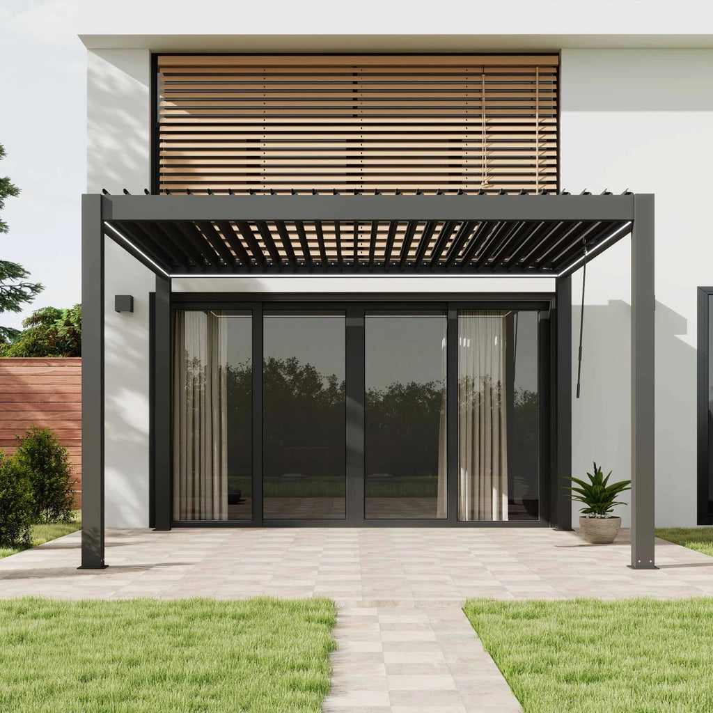 Modern black metal patio pergola with a slatted roof over a glass patio door, shown installed on a house exterior with a paved walkway, lawn, and wooden louvered wall above.