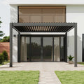 Modern black metal patio pergola with a slatted roof over a glass patio door, shown installed on a house exterior with a paved walkway, lawn, and wooden louvered wall above.