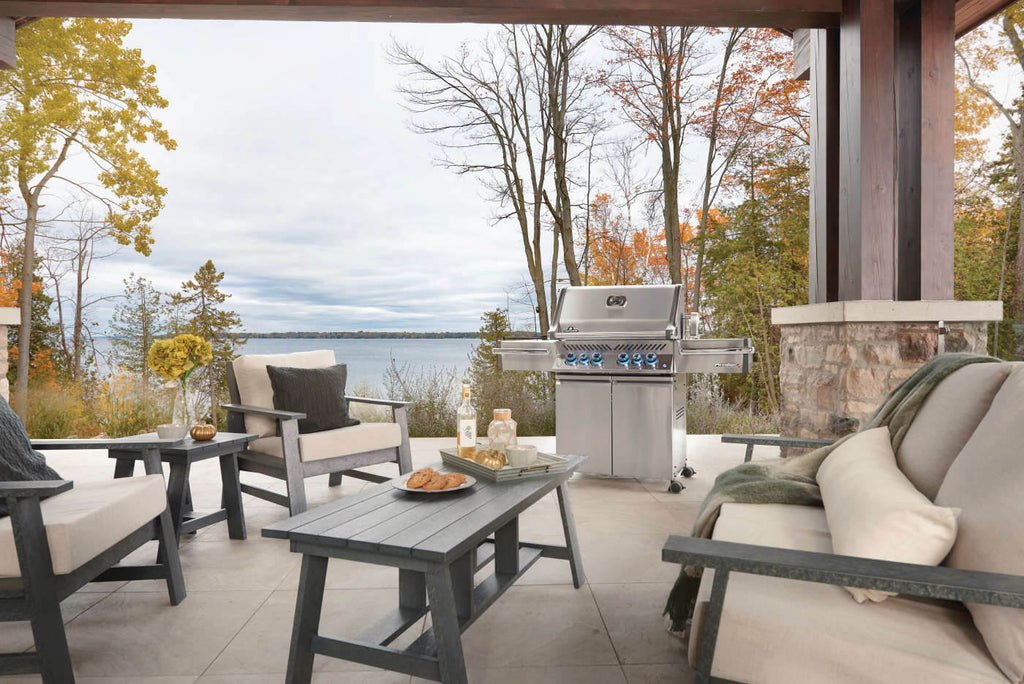 Outdoor patio with chairs, table, and grill overlooking a lake and trees.