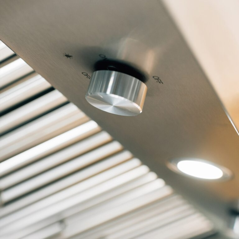 Vent hood with ceiling light fixture, control knob and blinds in the background