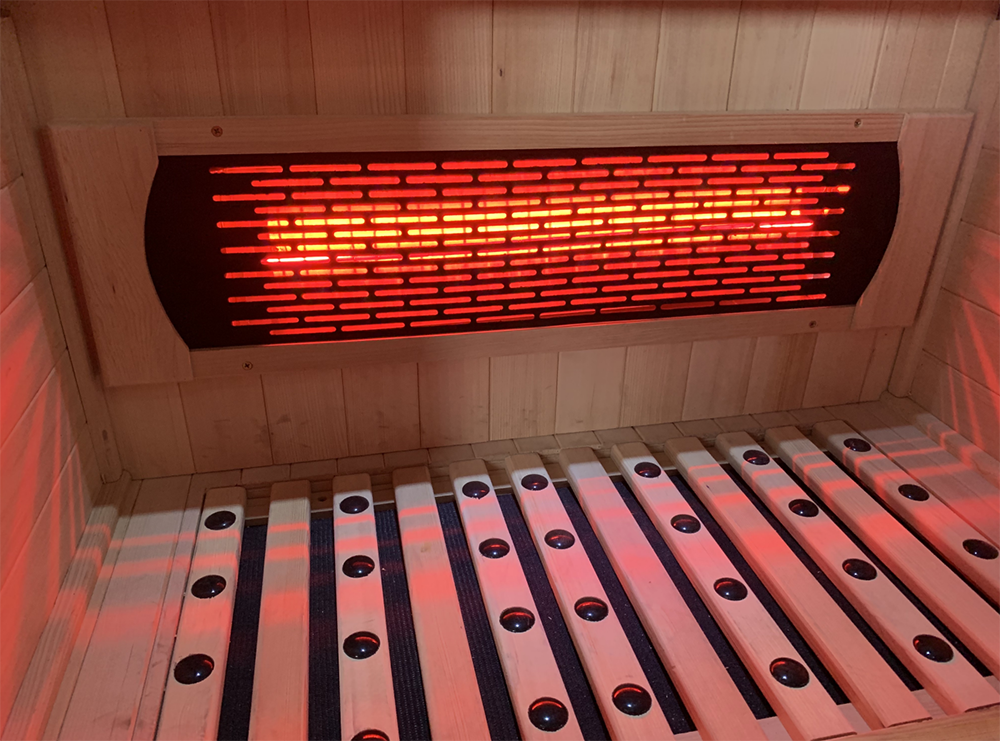 Infrared sauna with glowing heating element and wooden benches.