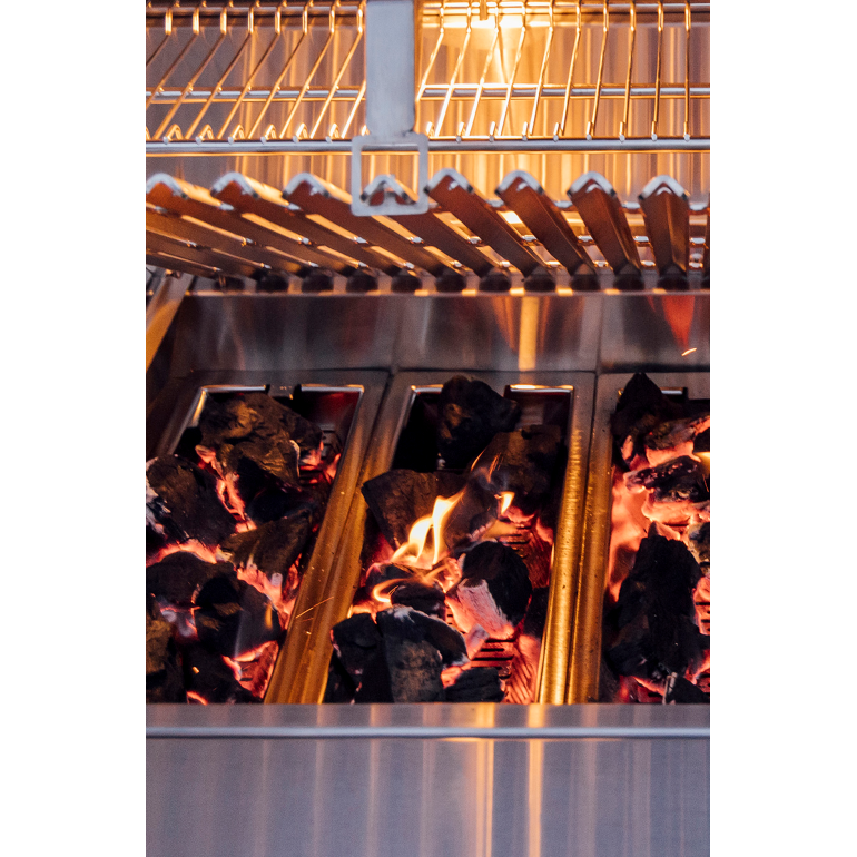 Close-up of a stainless steel charcoal grill with glowing embers and flames inside, under a metal grate.