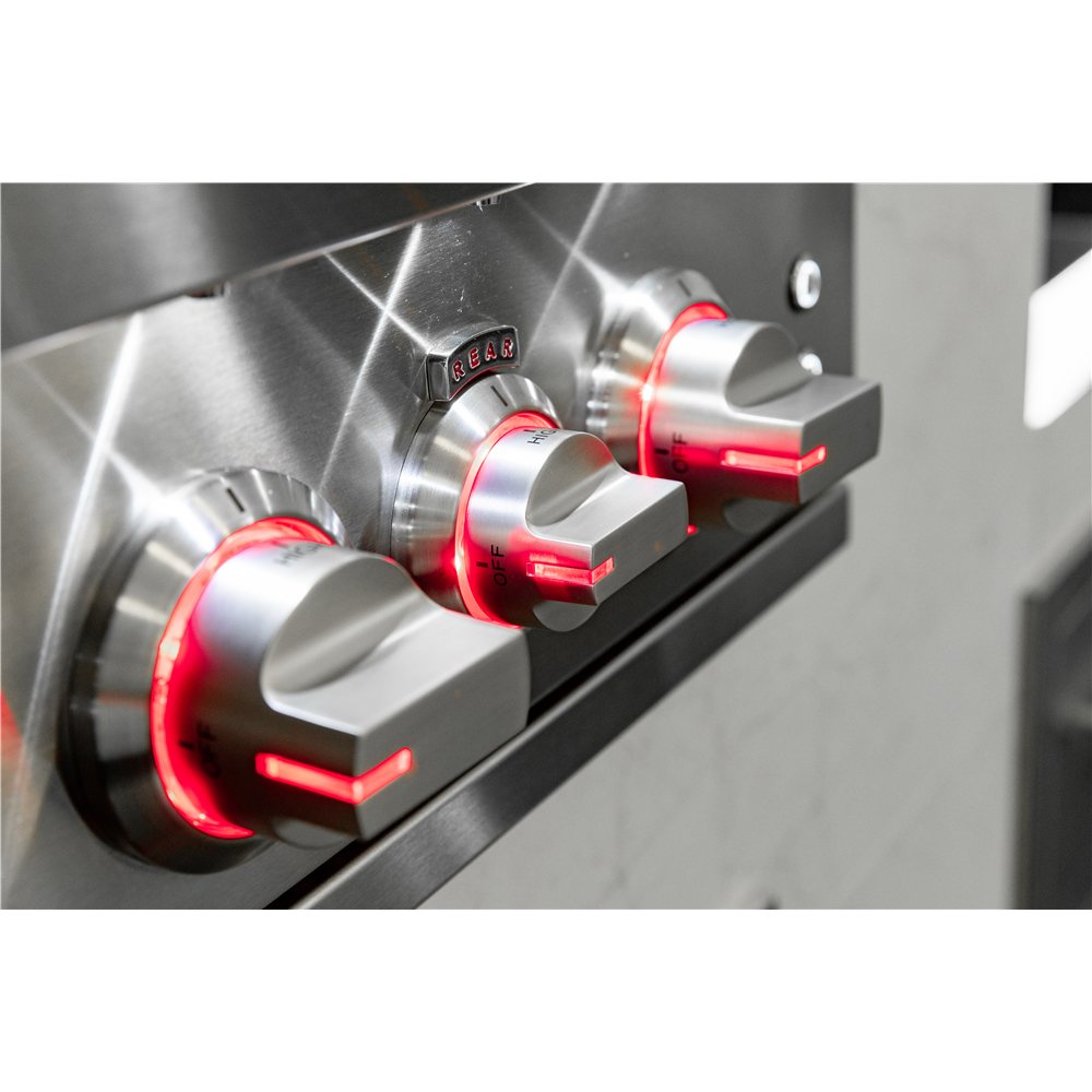 Close-up of stainless steel kitchen appliance control knobs with glowing red indicator rings and a small digital display.